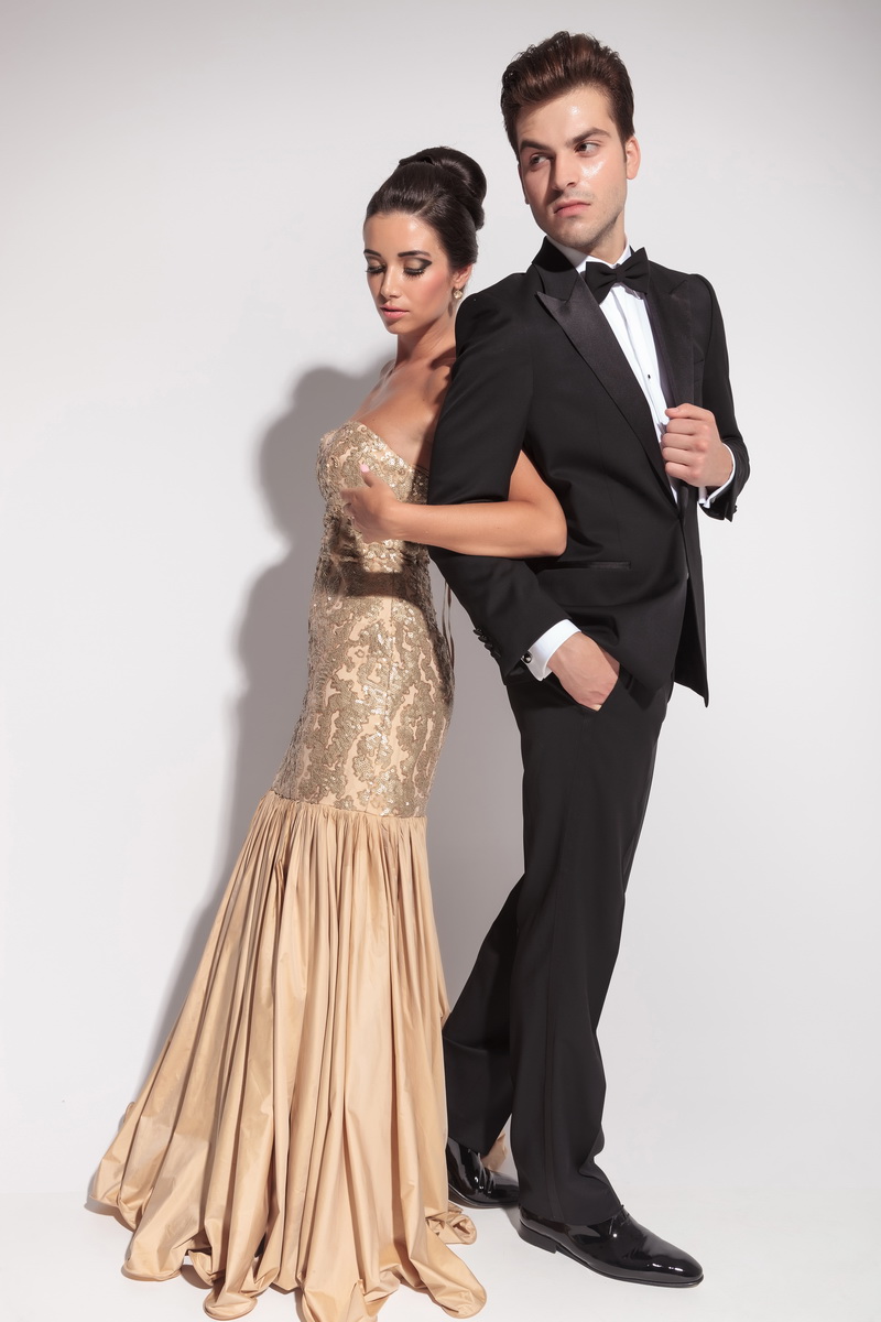 Full length picture of an elegant couple holding arms, looking away from the camera.