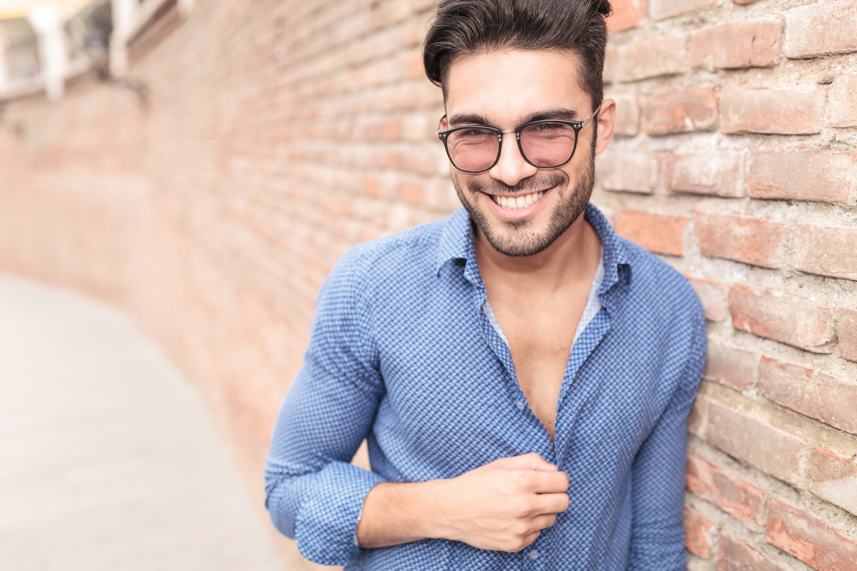 happy casual man leaning on brick wall laughs for the camera